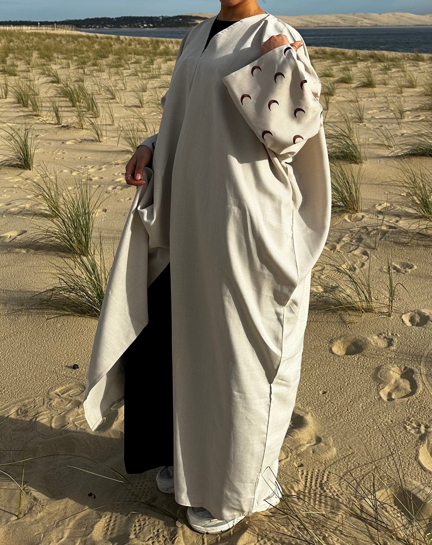 Découvrez notre abaya en lin beige, fabriquée à la main à Dubaï, avec des motifs lunaires marron brodés à la main le long des manches. Cette pièce unique incarne l'artisanat de luxe de Dubaï et offre un style authentique et élégant. Parfait pour ceux qui recherchent une mode haut de gamme, notre abaya en lin vous offre un mélange irrésistible de confort et de sophistication. Explorez notre collection dès aujourd'hui pour ajouter une touche de glamour oriental à votre garde-robe.
