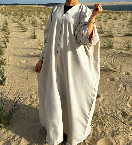 Découvrez notre abaya en lin beige, fabriquée à la main à Dubaï, avec des motifs lunaires marron brodés à la main le long des manches. Cette pièce unique incarne l'artisanat de luxe de Dubaï et offre un style authentique et élégant. Parfait pour ceux qui recherchent une mode haut de gamme, notre abaya en lin vous offre un mélange irrésistible de confort et de sophistication. Explorez notre collection dès aujourd'hui pour ajouter une touche de glamour oriental à votre garde-robe.